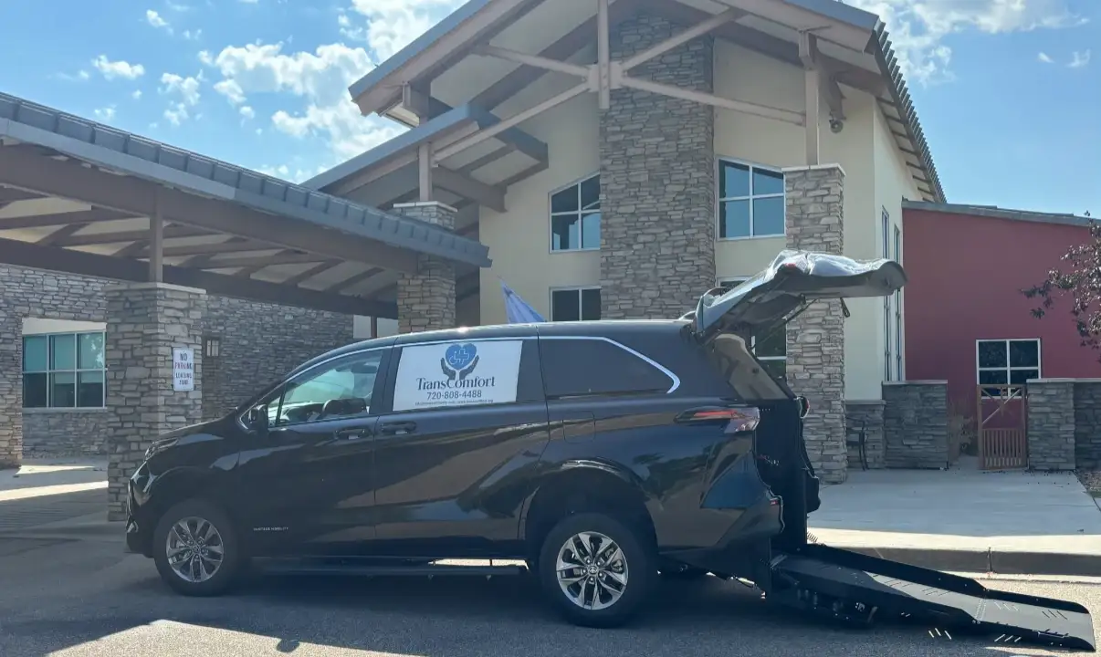 A TransComfort accessible van at a care-facility entrance with its rear ramp lowered to the pavement.